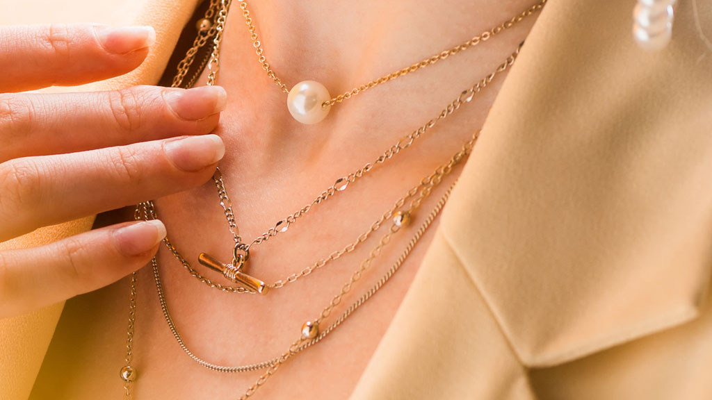 Quatre colliers à motifs différents disposés sur fond textile naturel illustrant les familles géométrique floral animalier abstrait