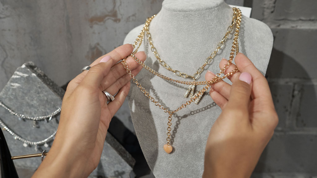 Femme essayant un collier à motifs avec expression pensive devant miroir